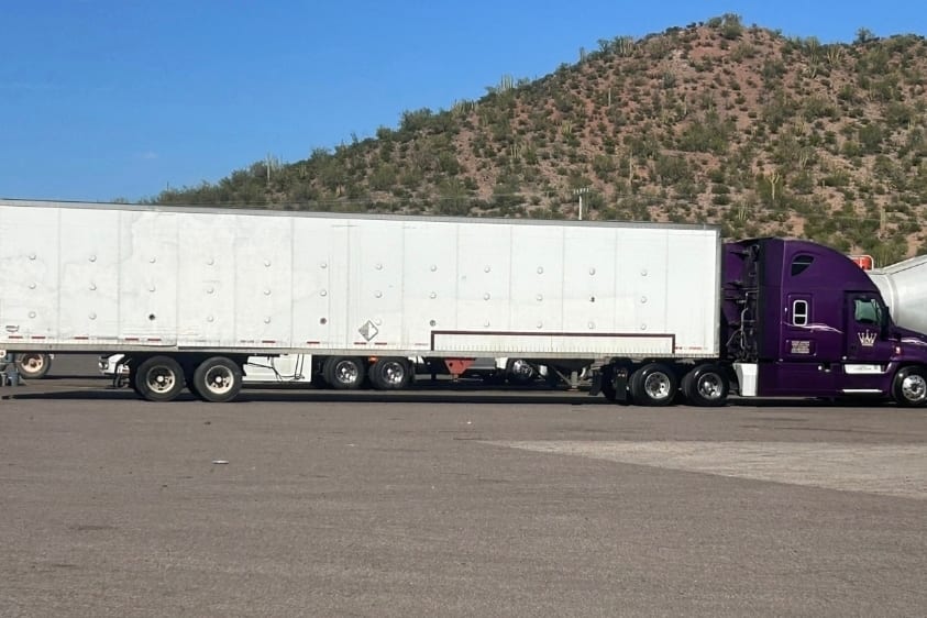 Tractocamión morado de Romo's Transportes conectado a una caja seca, en un entorno de carretera y montaña.