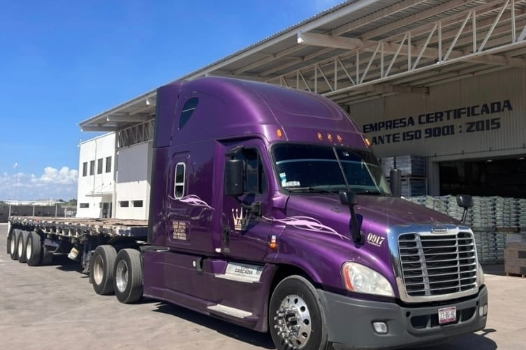 Tractocamión morado de Romo's Transportes con plataforma de tres ejes vacía, listo para cargar.