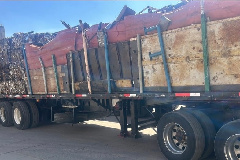 Plataforma con carga de material metálico cubierta y asegurada para su traslado.