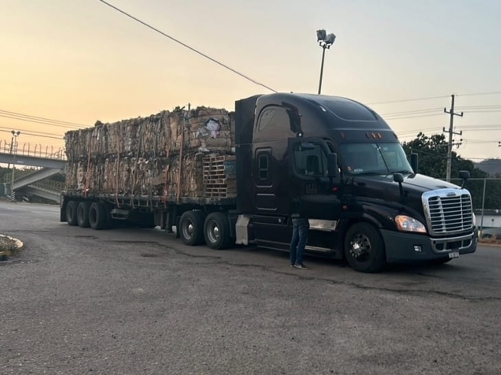 Tractocamión de Romo's Transportes con plataforma cargada de material enfardado, en operación al atardecer junto a una carretera.